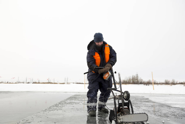 Рабочий вырезает ледяные блоки размером на льду замерзшего озера
 - Фото, изображение