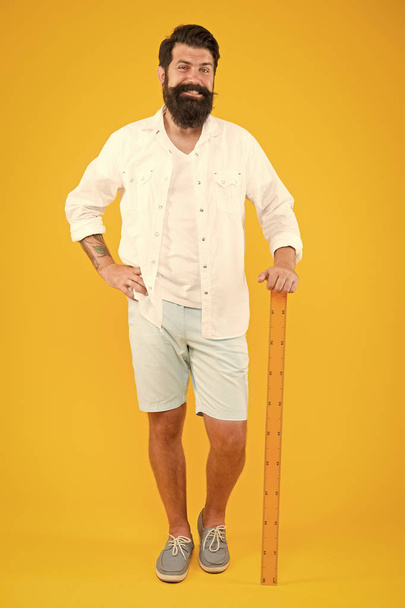 Back to class is here. Happy hipster holding ruler on yellow background. Brutal hipster smiling before maths and geometry lesson. Bearded man in trendy hipster style. Beardy hipster on September 1 - Fotografie, Obrázek