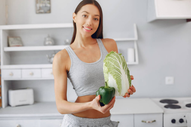 Beautiful and sporty girl in a kitchen with a vegetables - 写真・画像