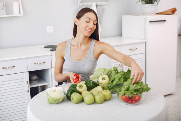 Beautiful and sporty girl in a kitchen with a vegetables - Photo, Image