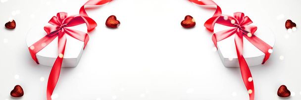 Composizione San Valentino: confezione regalo bianca con fiocco e cuore a nastro rosso, modello fotografico, sfondo. Vista dall'alto con spazio copia, romanticismo vacanza stagionale
 - Foto, immagini
