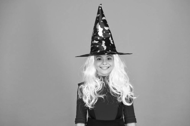 in holiday mood. magic fantasy. smiling girl halloween party. mystery witch. small child witch hat. trick or treat. supernatural charmer gray hair. kid enchantress orange background. happy halloween - Foto, afbeelding
