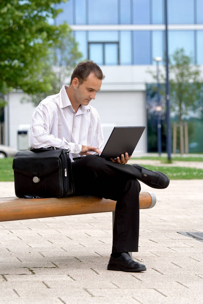 young businessman sitting on the bench and using laptop - Valokuva, kuva