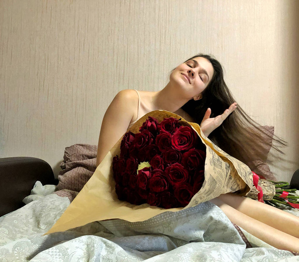 bella ragazza seduta a letto con un enorme mazzo di rose
. - Foto, immagini
