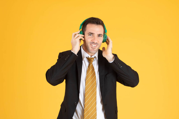 Portrait of confident businessman using headphone on yellow  bac - Zdjęcie, obraz
