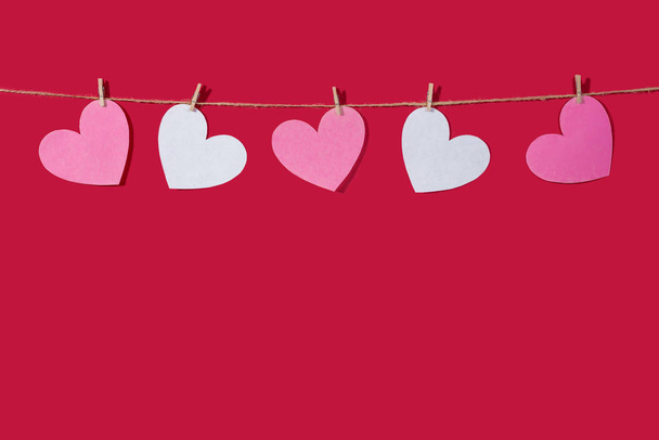 Garland of pink and white hearts on a red classic background. Natural rope and clothespins. Concept of Declaration of love, wedding, romantic relationship, Valentines Day. Copy space - Foto, imagen
