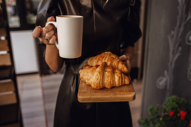 Close-up female hand serving hot latte and croissant in coffee s - Foto, afbeelding