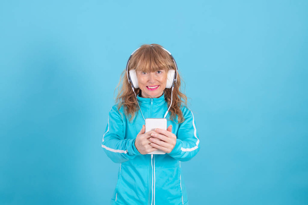 mujer adulta que usa ropa deportiva con auriculares y teléfono móvil aislado en el fondo de color
 - Foto, Imagen