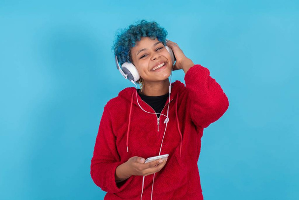 chica afroamericana con auriculares y teléfono móvil en color de fondo escuchando música
 - Foto, Imagen