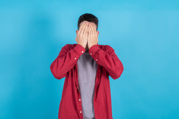молодой человек или студент-подросток, изолированный на цветном фоне с закрытым лицом и руками - Фото, изображение