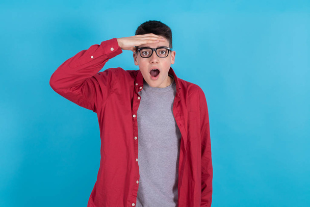 young man or teenage student isolated on color background with his hand in his eyes looking surprised - Foto, Imagen
