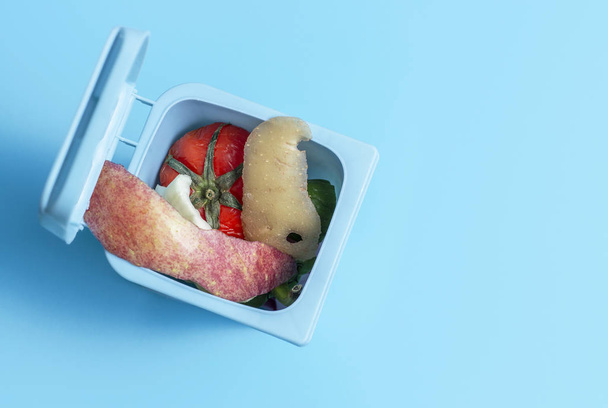 Mavi arkaplanda yiyecek atığı olan çöp kutusu, boşluk kopyala - Fotoğraf, Görsel