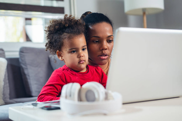 African American mother with little daughter using laptop together. - Фото, изображение