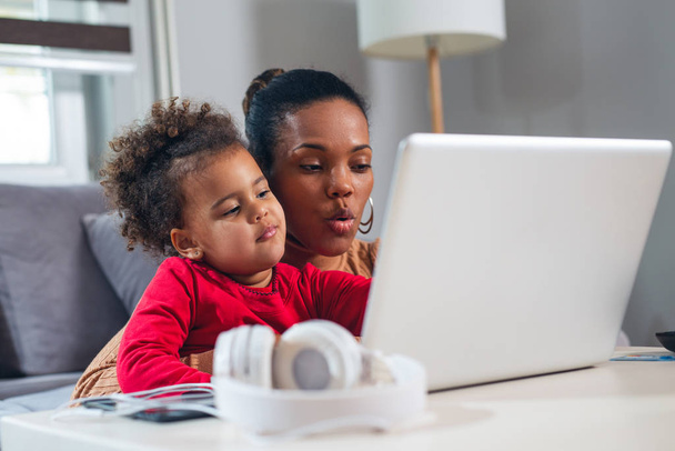 African American mother with little daughter using laptop together. - Фото, изображение