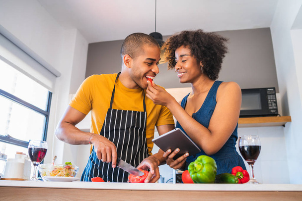 Латинская пара с помощью цифрового планшета во время приготовления пищи на кухне. - Фото, изображение