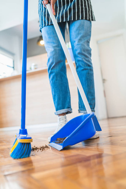 Latin man sweeping wooden floor with broom at home. - 写真・画像