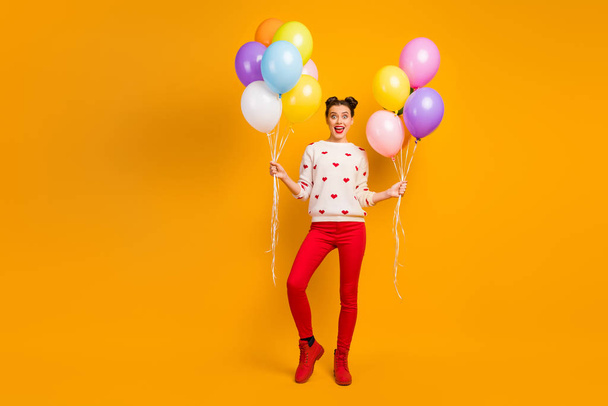 Surprise. Full body photo of beautiful lady bring many colorful air balloons friends event party wear hearts pattern sweater red pants shoes isolated yellow color background - Zdjęcie, obraz