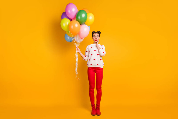 Full size photo of funny lady hold colorful air balloons open mouth unexpected surprise wear hearts pattern sweater red pants shoes isolated yellow color background - Photo, Image
