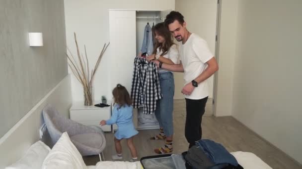 Happy caucasian family came back from vacation with their little daughter and unpacking the yellow suitcase in new house bedroom. Little girl walking around with globus ball. Bright, white walls room - Materiaali, video