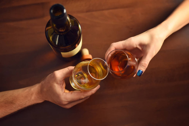 Ein Paar prostet mit zwei Gläsern Whisky auf einem Holztisch zu - Foto, Bild