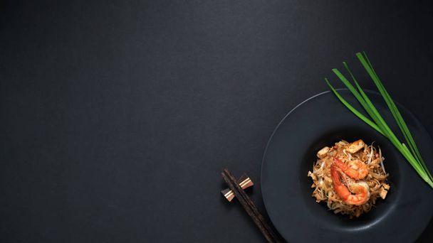 Top view of Pad Thai, stir fly of Thai noodle with shrimp and egg in black ceramic plate with copy space on black table  - Foto, immagini