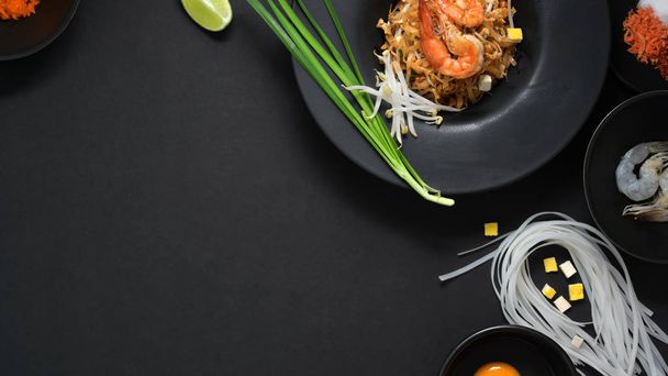 Vista superior de Pad Thai, revuelva la mosca de fideos tailandeses con camarones, huevo, ingredientes y condimento con espacio para copiar en placa de cerámica negra en la mesa negra
  - Foto, imagen