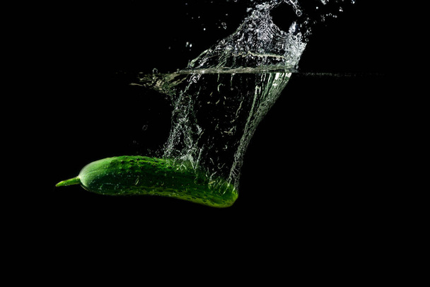 Fresh green cucumber in water with splash on black background - Foto, afbeelding