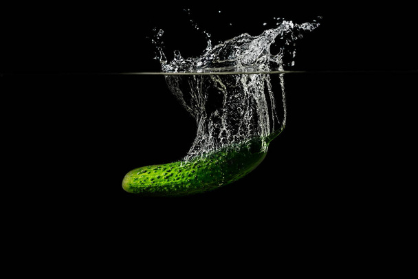 Fresh green cucumber in water with splash on black background - Photo, Image