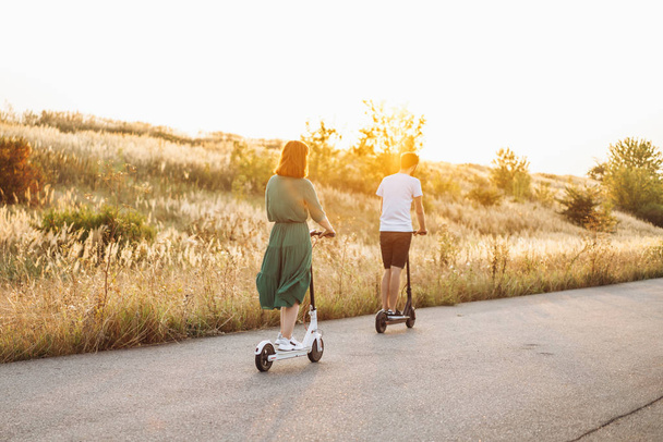 junges Paar im Urlaub, das Spaß am Fahren von Elektrorollern auf der Straße in der Natur hat. Content-Technologien. zurück - Foto, Bild
