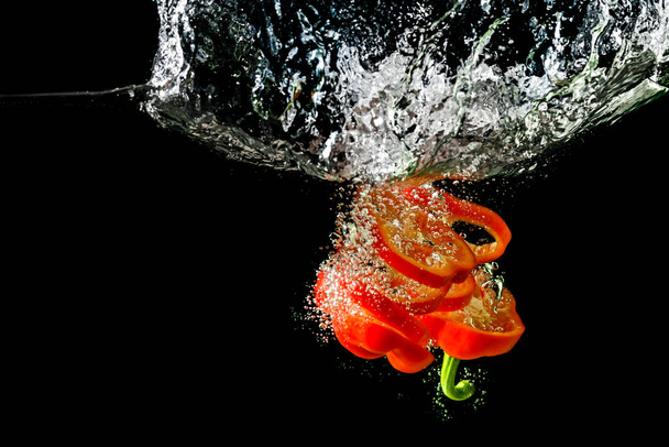 Red fresh paprika slices splash in water on a black background. Food concept. - Фото, зображення
