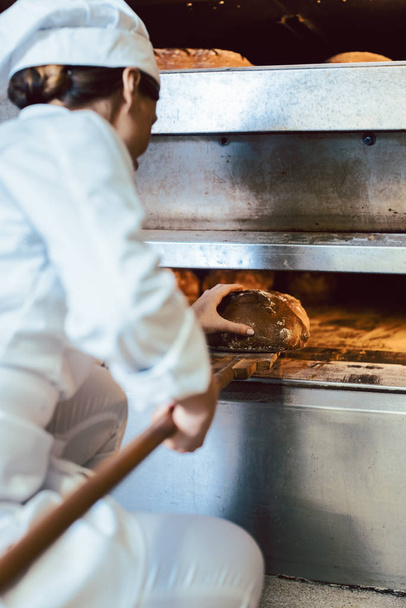 Baker putting bread in the bakery oven - Fotoğraf, Görsel