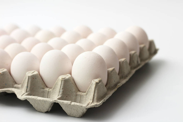 Una bandeja aislada de huevos de materiales reciclados con huevos blancos sobre un fondo blanco. Enfoque selectivo
 - Foto, imagen