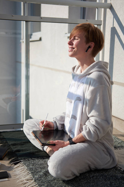 Руда біла дівчина сидить на плетеному балконі з планшетом
 - Фото, зображення