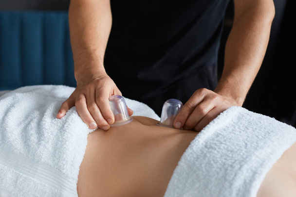 Young beautiful woman enjoying cupping massage in spa.Professional massage therapist is treating a female patient in apartment.Relaxation,beauty,body and face treatment concept.Home massage - Photo, Image