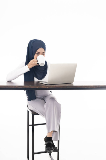 Asian young adult woman wearing hijab using laptop and sipping coffee search and doing office work isolated in white background - office, business, finance and work station concept - Фото, изображение