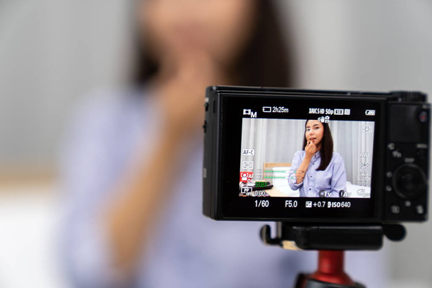 Young beautiful Asian woman beauty vlogger or blogger recording live how to make up tutorial to share on social media using digital camera on table tripod. Using for vlog social media influencer concept. Focus on camera. - Foto, imagen