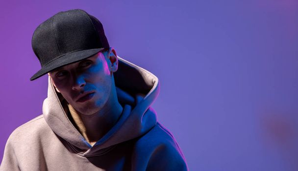 Men portrait in a neon light. Beneath in the hoodie and hat. Dark face. Hip-hop style. - Photo, Image