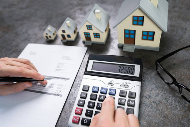 Businessman Calculating Tax By Small And Big House Models - Foto, Imagen