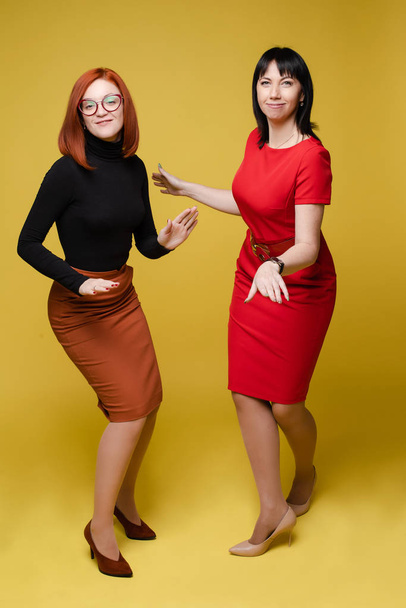 Two women in dresses and heels dancing on yellow background. - 写真・画像