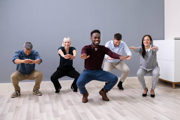 Smiling Multi Ethnic Young Businesspeople Doing Sit-ups Together At Workplace - Photo, Image
