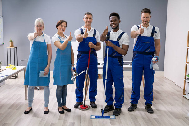 Portrait Of Happy Diverse Janitors In The Office With Cleaning Equipment Showing Thumb Up Sign - Foto, Imagem