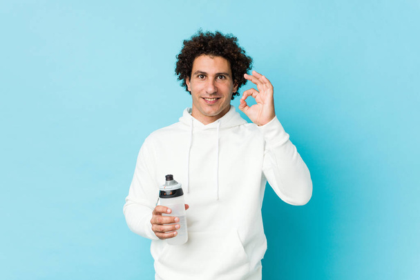Sport man holding a water bottle cheerful and confident showing ok gesture. - Fotoğraf, Görsel