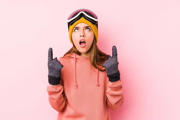 Młoda kobieta rasy kaukaskiej w odizolowanych ubraniach narciarskich skierowanych do góry nogami z otwartymi ustami. - Zdjęcie, obraz