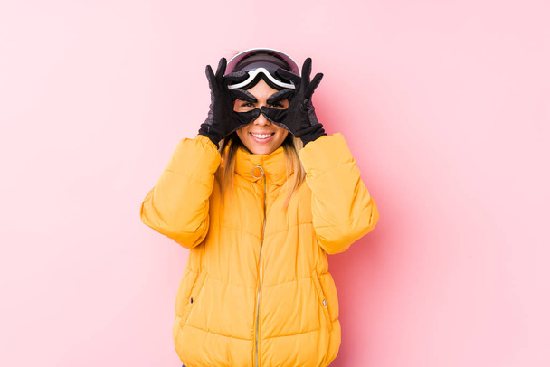 Νεαρή Καυκάσια γυναίκα που φοράει ρούχα του σκι σε ροζ φόντο που δείχνει εντάξει σημάδι πάνω από τα μάτια - Φωτογραφία, εικόνα