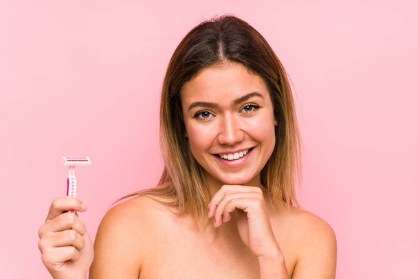 Young caucasian woman holding a razor blade isolated Young caucasian woman holding a hairbrush isolated happy, smiling and cheerful. - Photo, image