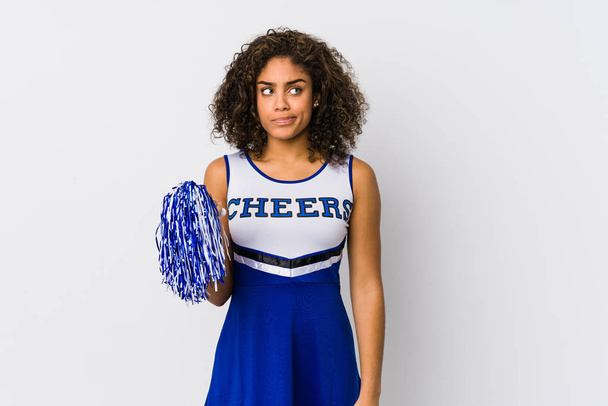 Young african american cheerleader woman isolated confused, feels doubtful and unsure. - 写真・画像