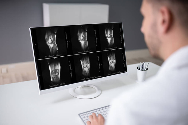 Mature Male Doctor Examining Knee X-ray In Clinic - Foto, Imagem