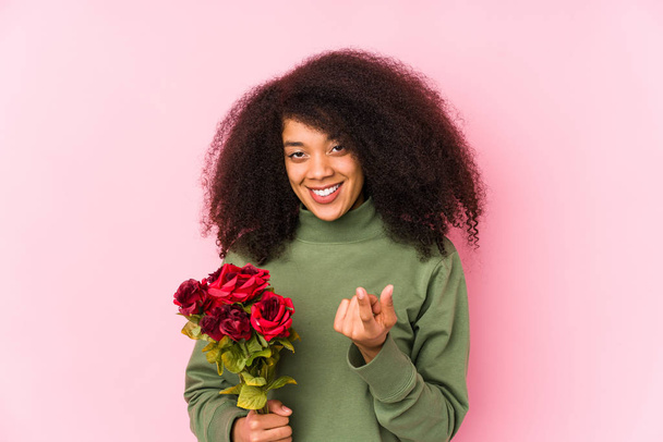 Joven mujer afro sosteniendo una rosa aislada Joven mujer afro sosteniendo una rosa señalándote con el dedo como si invitaras a acercarte
. - Foto, Imagen