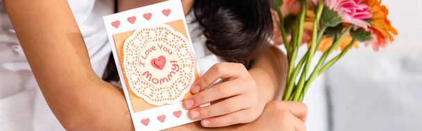 bijgesneden weergave van kind knuffelen moeder terwijl het houden van moeders dagkaart met ik hou van je mama inscriptie, panoramisch schot  - Foto, afbeelding