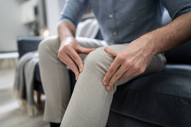 Man Suffering From Knee Pain Sitting On Sofa - Photo, image
